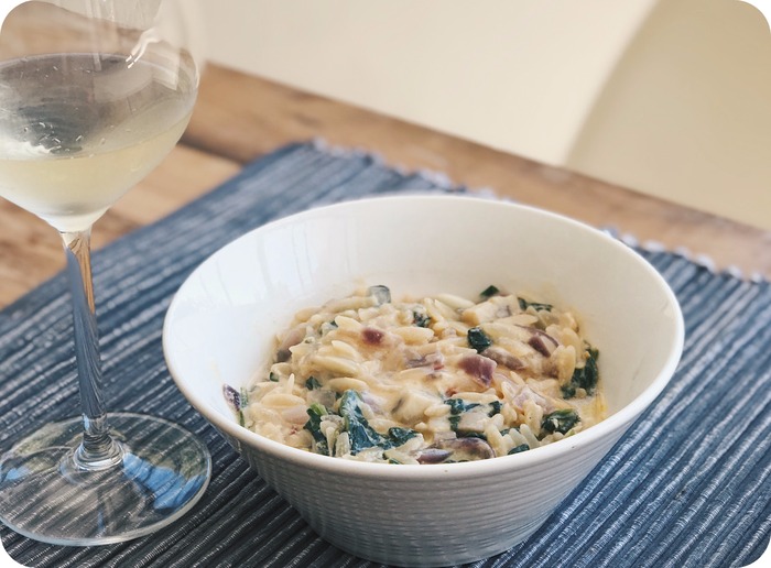 Creamy lemon spinach mushroom orzo soup served in a bowl with glass of white wine