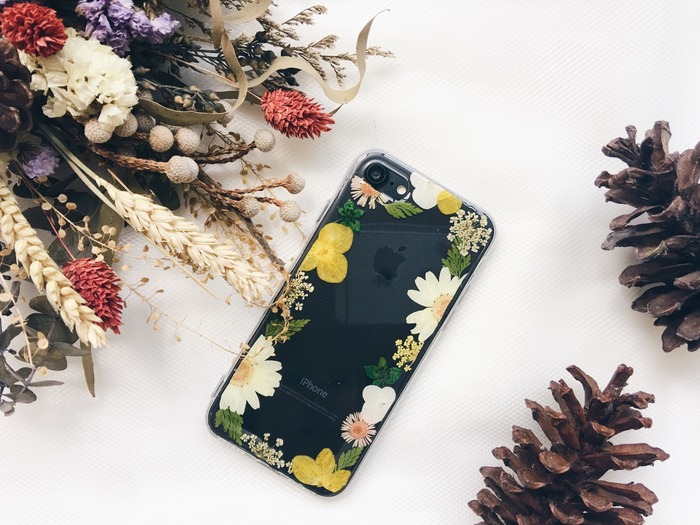 Yellow pressed flowers phone case against black phone